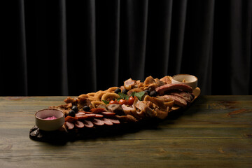 assorted meats on a wooden base with sauces and tomatoes