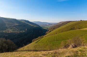 Fototapeta premium Springtime countryside scene with farmland, valleys, and rolling hills. A narrow, deep chasm with sharp inclines. A raised terrain that's smooth and not as rough as a mountain.
