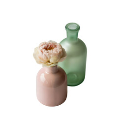 Pink ceramic vase with a blush peony flower next to a frosted mint green glass bottle isolated on transparent background.