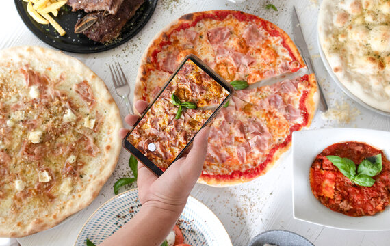 Person photographing pizza and italian food with smartphone