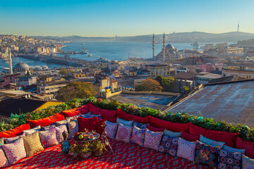 Fototapeta premium Magnificent panoramic views of Istanbul from the rooftop with a traditional Turkish carpet, pillows, hookah and a fruit table.