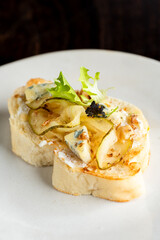 Pear and blue cheese crostini appetizer on a white plate. Gourmet finger food with fresh ingredients and a focus on texture and detail.