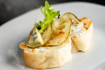 Pear and blue cheese crostini appetizer on a white plate. Gourmet finger food with fresh ingredients and a focus on texture and detail.