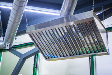 Stainless steel exhaust hood with grease trap close-up in a large industrial kitchen in the...