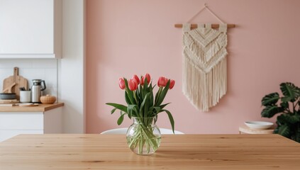 Contemporary bohemian and Scandinavian open-plan kitchen featuring white surfaces, a wooden counter adorned with pink tulip blossoms in a vase, and macrame wall art. Inviting and chic home styling.