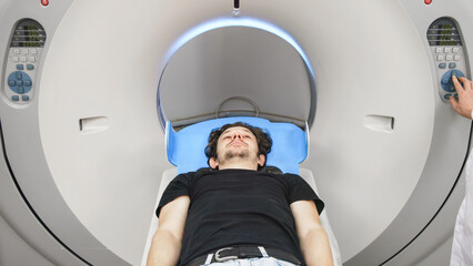 Patient lying on CT scanner table, preparing for tomography procedure, with medical staff adjusting settings, showcasing advanced x-ray diagnostic technology in a clinical environment