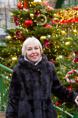 A smiling white woman with short hair stands by a decorated Christmas tree. She's wearing a black...