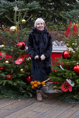 A smiling white woman with short hair stands by a decorated Christmas tree. She's wearing a black...