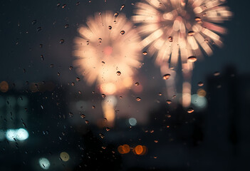 Raindrops on glass with blurred fireworks and city lights at night