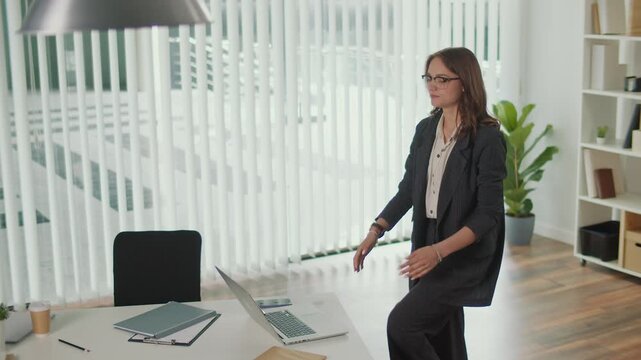 Productivity Hacks and Healthy Workplace. Office Manager Performs Standing Lumbar Spine and Hip Stretch at Desk to Boost Energy, Improve Posture, Prevent Back Pain, Support Work Life Balance and Focus