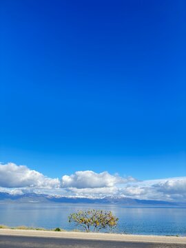 Calm waters mirror the snow-dusted mountains and drifting clouds beneath a brilliant blue sky, capturing the peaceful harmony of nature where earth, water, and sky unite in quiet perfection.