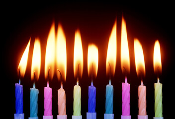 Many colourful birthday cake candles burning on black background