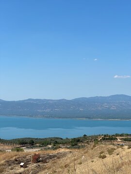 A serene panoramic view of a turquoise lake surrounded by lush green hills and distant blue mountains under a clear summer sky, capturing the calm beauty of untouched nature in perfect harmony.