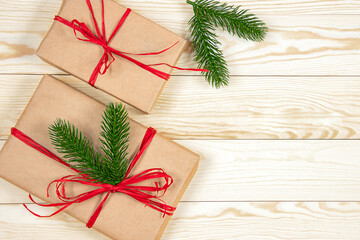 Two kraft paper gift boxes with red ribbons on a light wooden surface. Each box is decorated with a green pine branch.