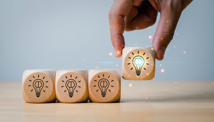 Creative innovation concept glowing light bulb with brain symbol on wooden block hand picking unique idea leadership inspiration creativity success motivation teamwork