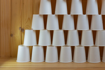 White paper cups stacked in a pyramid on a wooden background