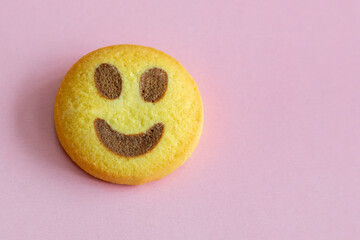 Shortbread cookie shaped like a smiley emoji lies on a light pink background, macro shot.