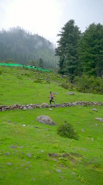 Defocused Indian man running in front of the Himalayan mountain ranges covered with clouds during the monsoon season near Udaipur in Pattan Valley, Lahaul, Himachal Pradesh, India.