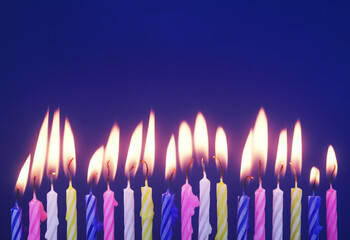 Colourful birthday cake candles burning on blue background