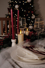 A festive holiday table setting with lit candles, wine glasses, and a Christmas tree in the background