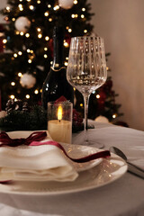 A festive holiday table setting with lit candles, wine glasses, and a Christmas tree in the background
