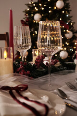A festive holiday table setting with lit candles, wine glasses, and a Christmas tree in the background
