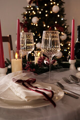 A festive holiday table setting with lit candles, wine glasses, and a Christmas tree in the background