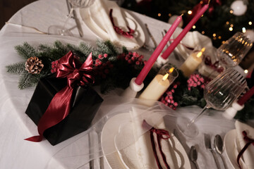 A festive holiday table setting with lit candles, wine glasses, and a Christmas tree in the background