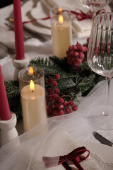 A festive holiday table setting with lit candles, wine glasses, and a Christmas tree in the background
