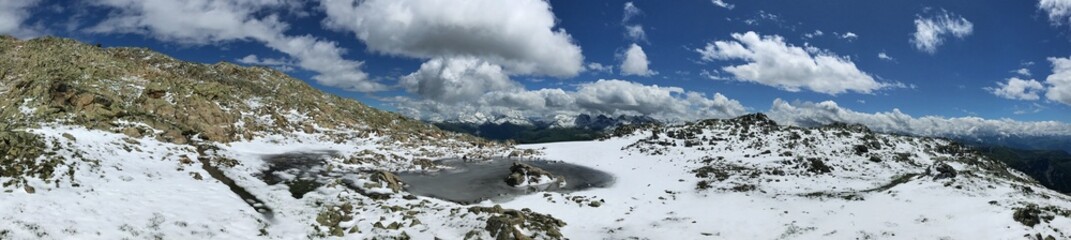 Snowy mountain landscape panorama with small frozen lake and clear blue sky