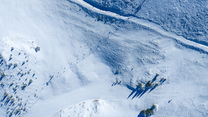 Aerial view of untouched snowy landscape with shadows of trees and footprints crossing frozen terrain