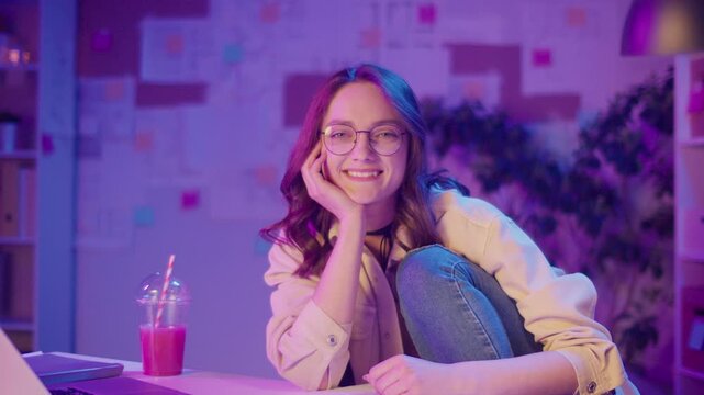 Empowered Learning, Academic Confidence, Digital Era. Student Sits in Relaxed Pose and Looks at Camera in Neon Room. A Portrait of Focus, Authenticity, and the New Face of Education