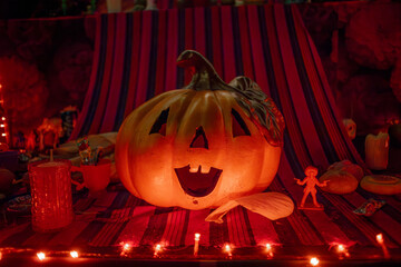 Illuminated carved pumpkin Jack-o'-lantern on a festive Day of the Dead altar or display, with atmospheric red lights.