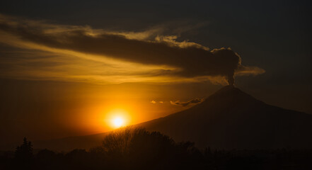 Stunning silhouette of Popocatépetl volcano erupting during a vibrant sunset. Fumarole and ash emerging under a dramatic sky in Mexico.