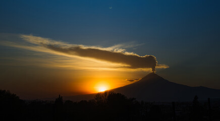 Stunning silhouette of Popocatépetl volcano erupting during a vibrant sunset. Fumarole and ash emerging under a dramatic sky in Mexico.