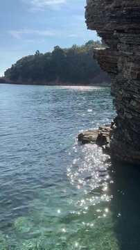 Scenic shoreline view with sparkling water and rocky cliff, camera pans right