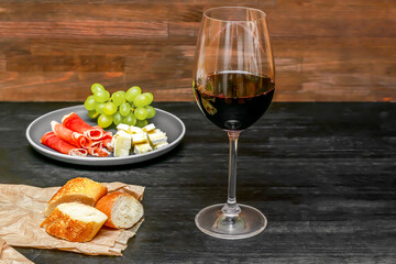 Red wine in glass,brie cheese,grapes,jamon meat,salami on slate board wooden table,alcohol drink with snacks,food banner, still life