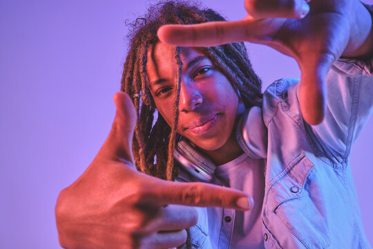 Young person with dreadlocks and headphones framing view with hands under neon light