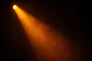 Orange stage spotlight beam cutting through dark atmosphere. Dramatic lighting for concert or theater creates mysterious and focused mood, highlighting an empty space