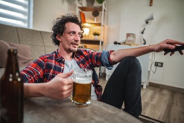 Man relaxing on sofa, drinking beer and watching tv