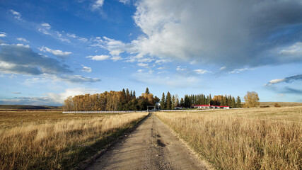 Fototapeta premium Dirt Road Leading to a Remote Ranch with a Red Roof in an Autumn Landscape