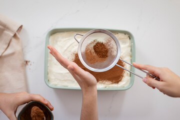 A hands sprinkling chocolate on dessert, tiramisu.