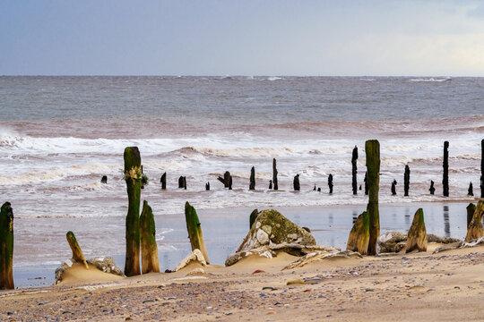 Stormy Spurn Head shoreline with weathered wooden groynes, North Yorkshire, UK.