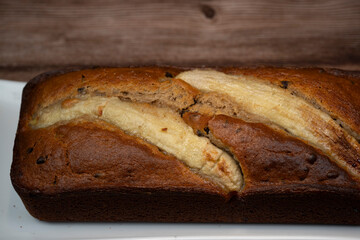 Sliced banana bread rests on a white plate, showing its rich brown color and golden crust. The sweet aroma fills the air, inviting everyone to enjoy this delicious treat.