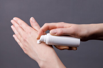 Applying hand cream for moisturizing and skincare, Close-up of woman’s hands applying moisturizing cream from white dispenser bottle onto skin, focusing on personal care and hygiene.