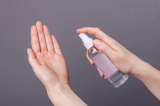 Applying disinfectant spray on hands for hygiene care, Close-up of a person spraying disinfectant or sanitizer onto hand, promoting cleanliness, skincare, and personal hygiene on gray background.