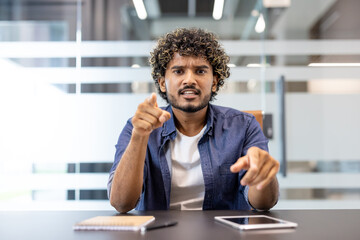 Portrait of a young angry Indian man sitting in the office facing the camera and talking emotionally