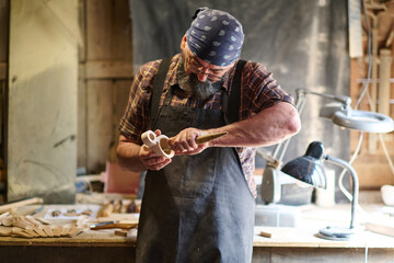 Craftsman shaping wooden toy in workshop, artisan carving wood, handmade crafts, woodworking,...