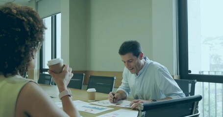 Two colleagues marking printed charts and holding coffee cup in boardroom, with city skyline