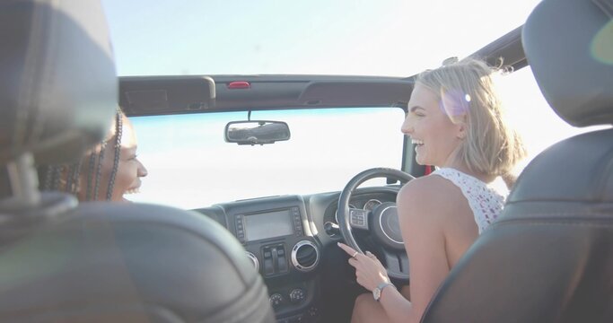 Driving two women wearing tops, smiling in convertible on road, with steering wheel
